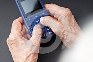Old wrinkled hands holding a push-button mobile phone with big buttons.