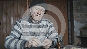 Old wrinkled man hewing handmade wooden spoon as present for wife 4K