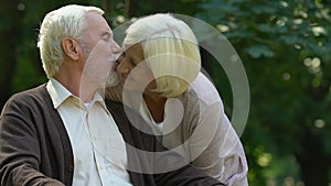 Old wrinkled man and woman kissing with tenderness in park, happiness and love