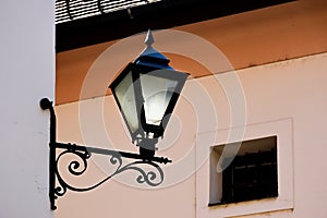 Old wrought iron street light lantern. ornate retro stile lamp. stucco facade.