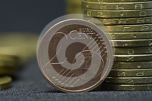 An old, 2009 year, two euro cent coin put on edge in front of piles of coins