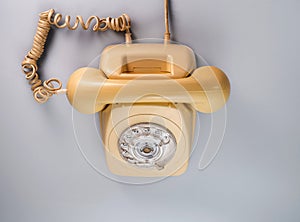 Old yellow antique rotary telephone on blue background. Vintage landline home phone with dial, twisted cable and