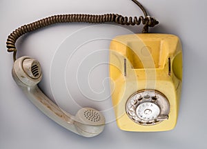 Old yellow antique rotary telephone with grey removed receiver on blue background. Vintage landline home phone with dial