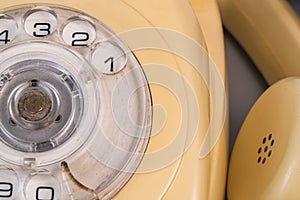 Old yellow antique rotary telephone with removed handset receiver on grey background. Vintage landline home phone with