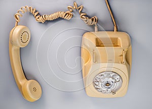 Old yellow antique rotary telephone with removed receiver on blue background. Vintage landline home phone with dial