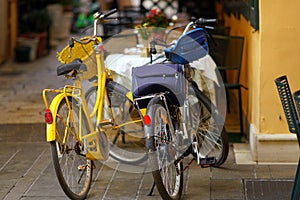 An old yellow bicycle and a modern black electric bicycle parked in a narrow street of Corfu