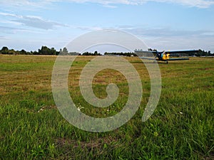 An old yellow biplane with blue wings and a running engine drives through a field of green grass