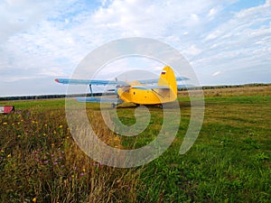 An old yellow biplane with blue wings and a running engine drives through a field of green grass
