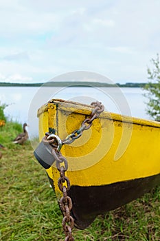 An old yellow boat chained up on the lake shore in summertime