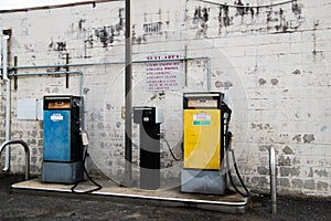 Old yellow diesel pump and old blue gasoline pump in front of old white brick wall