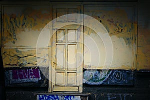 An old yellow door against a wall of the same color and a dark blue baseboard.