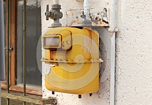 Old yellow gas meter hanging on a wall outdoors