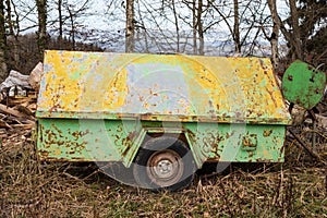 Old yellow green tool trailer with wheel and lots of rust in cloudy weather