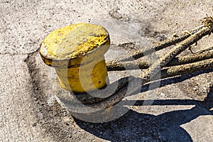 Old yellow mooring bollard with heavy duty mooring ropes on a berth