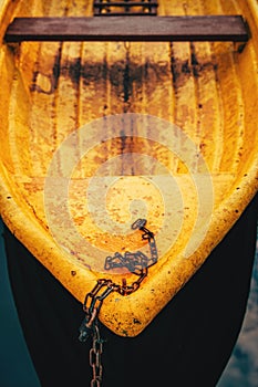 Old yellow plastic dinghy fishing boat with rusty chain, selective focus