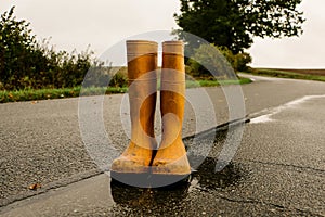 Old yellow rubber boots stand in a puddle on the street