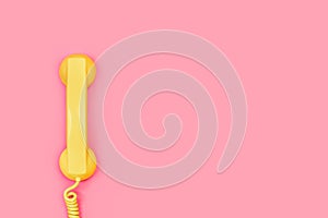 An old yellow telephone receiver on a pink background