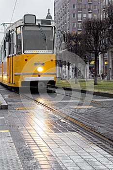 Old yellow tram on gray city street. Urban vintage train. Transport and travel concept. City tram in Budapest.