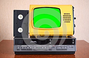 An old yellow vintage TV with a green screen to add new images to the screen, a VCR in the background of the wallpaper.