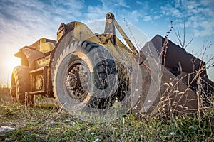 Old yellow wheel loader left in the field, view from the ground.