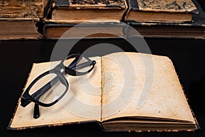 Old yellowed book and black glasses. Forgotten publications on the dark table