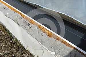 Old yellowed mounting foam under a large terrace window, visible styrofoam insulating the foundations of the house.