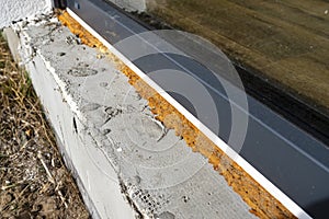 Old yellowed mounting foam under a large terrace window, visible styrofoam insulating the foundations of the house.