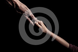 Old and young hands together on a black background holding hands