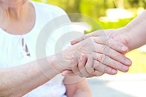 Old and young holding hands on light background close up. Helping hands, care for the elderly concept.