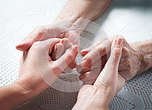 Old and young holding hands on light background, closeup. Care is at home of elderly