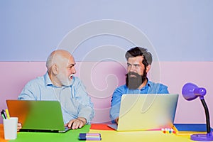 Old and young men looking at laptop screen watching movie or news in social network. Two business people. Business