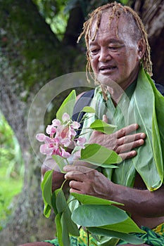 Olde aged Pacific Islander man looks at exotic flower on eco tourism tour in Rarotonga Cook Islands