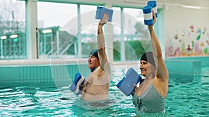 Older adults man and woman doing aquatic exercises with foam dumbbells in the swimming pool