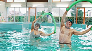 Older adults man and woman doing aquatic exercises with water noodles in the swimming pool