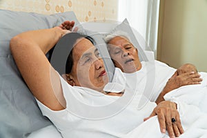 Older Asian woman laying open her eyes in bed beside her husband who snores and Makes noise, Marital problems