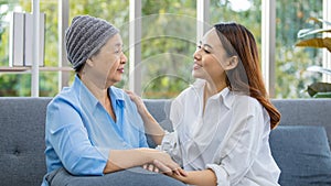 Older Asian woman patient covered the head with clothes effect from chemo treatment in cancer cure process hold hands of daughter photo