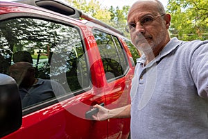 An older bald Caucasian male with his hand on the handle of a red sport utility vehicle