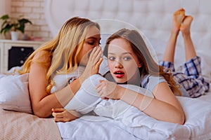 Older blonde-haired sister whispering something to cute sibling