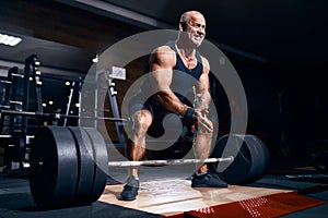 Older bodybuilder preparing to exercise deadlift with barbell while on cross training in a gym.