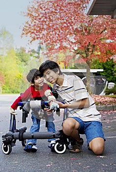 Older brother helping little disabled boy walk in walker outdoors photo