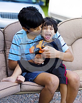 Older brother holding disabled little boy on lap outdoors
