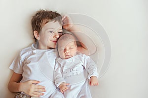 Older brother hugging his newborn sister. Children in bright clothes on a white blanket.