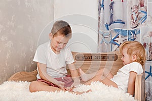 Older brother tickles younger sister`s bare feet on bed at home