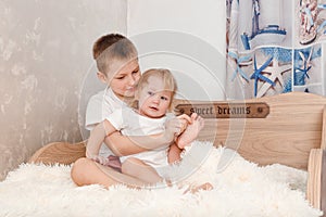 Older brother tickles younger sister`s bare feet on bed at home