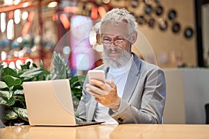 Older business man executive using mobile phone working late in office.