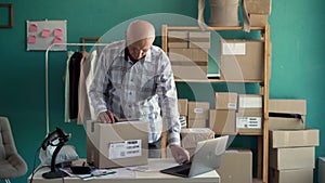 Older businessman entrepreneur, clothing seller using laptop checking e-commerce order packing in online shop