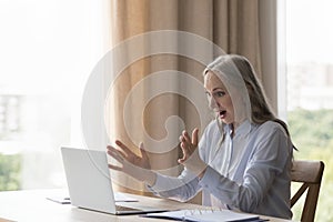 Older businesswoman open mouth gawp at laptop screen feels shocked