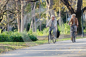 Older Caucasian couple riding bicycles through public park together