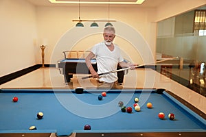 Older caucasian men, white beard and white hair in white shirt looking at billiard or snooker ball with concentration and serious
