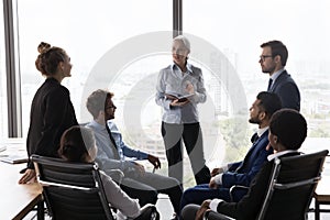 Older company boss leads briefing with young staff in office